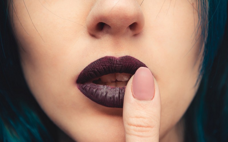 Девушка прикасается пальцем к левому уголку губы