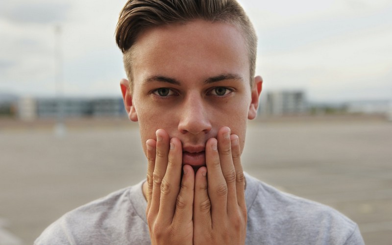 Парень прикладывает ладони к губам