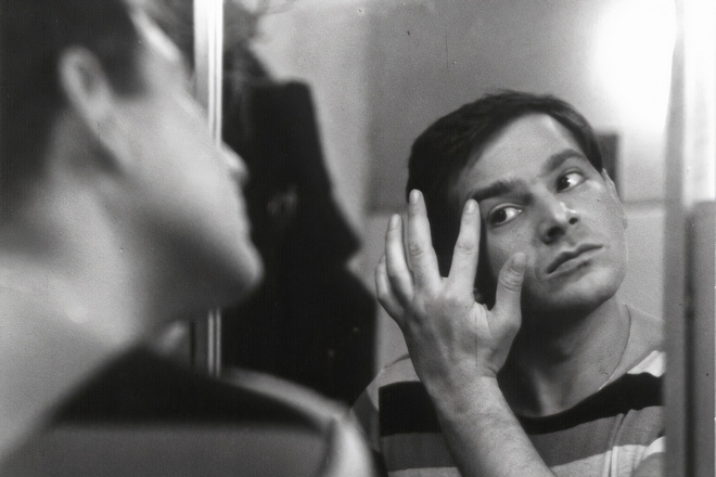 Мужчина рассматривает в зеркало прыщик возле левого глаза