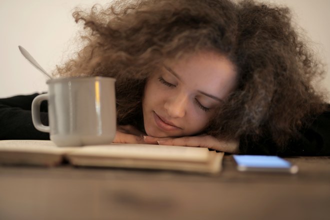 Девушка спит возле книжки и чашки