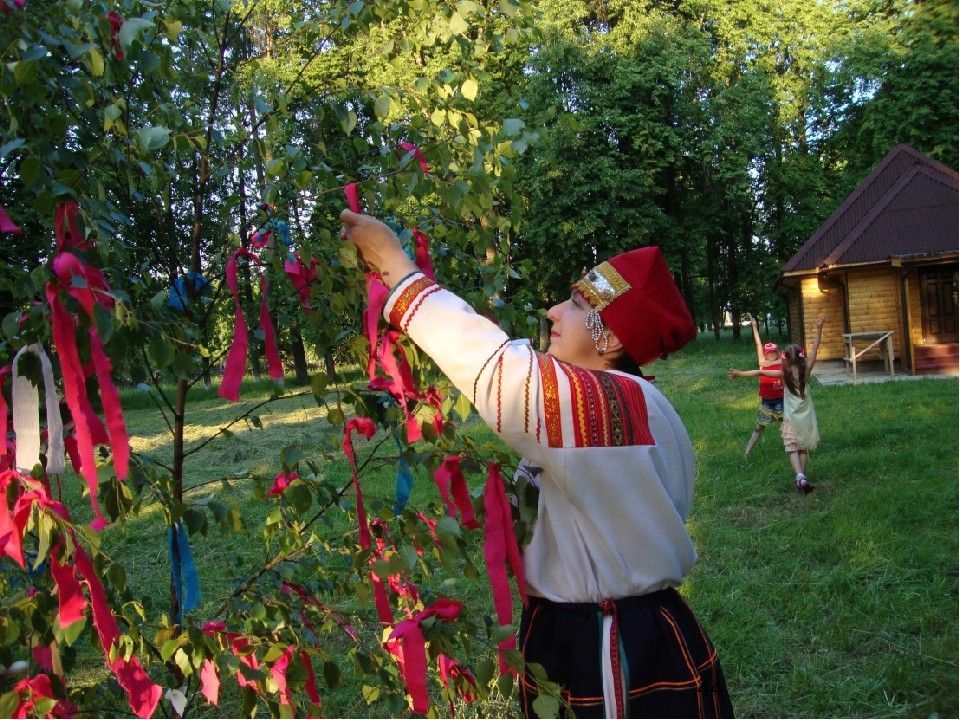 Девушка привязывает красную ленту на березу