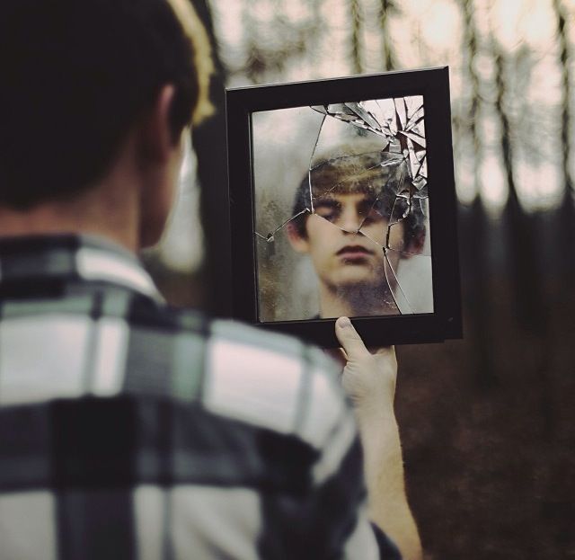 молодой человек держит в руках разбитое зеркало